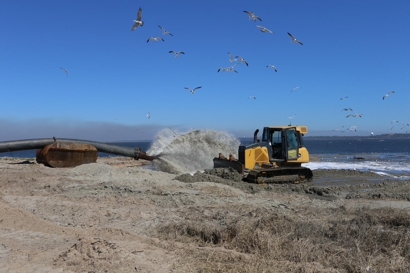 A bulldozer flattens sand as its pumped onto an island.