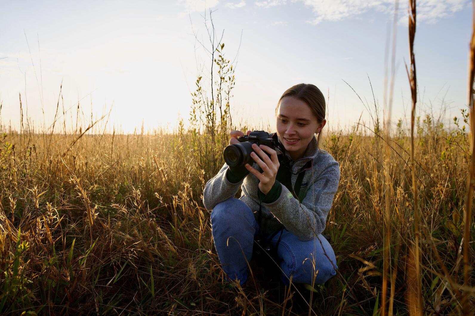 Brittany crouching in a field of grass photographing researchers 